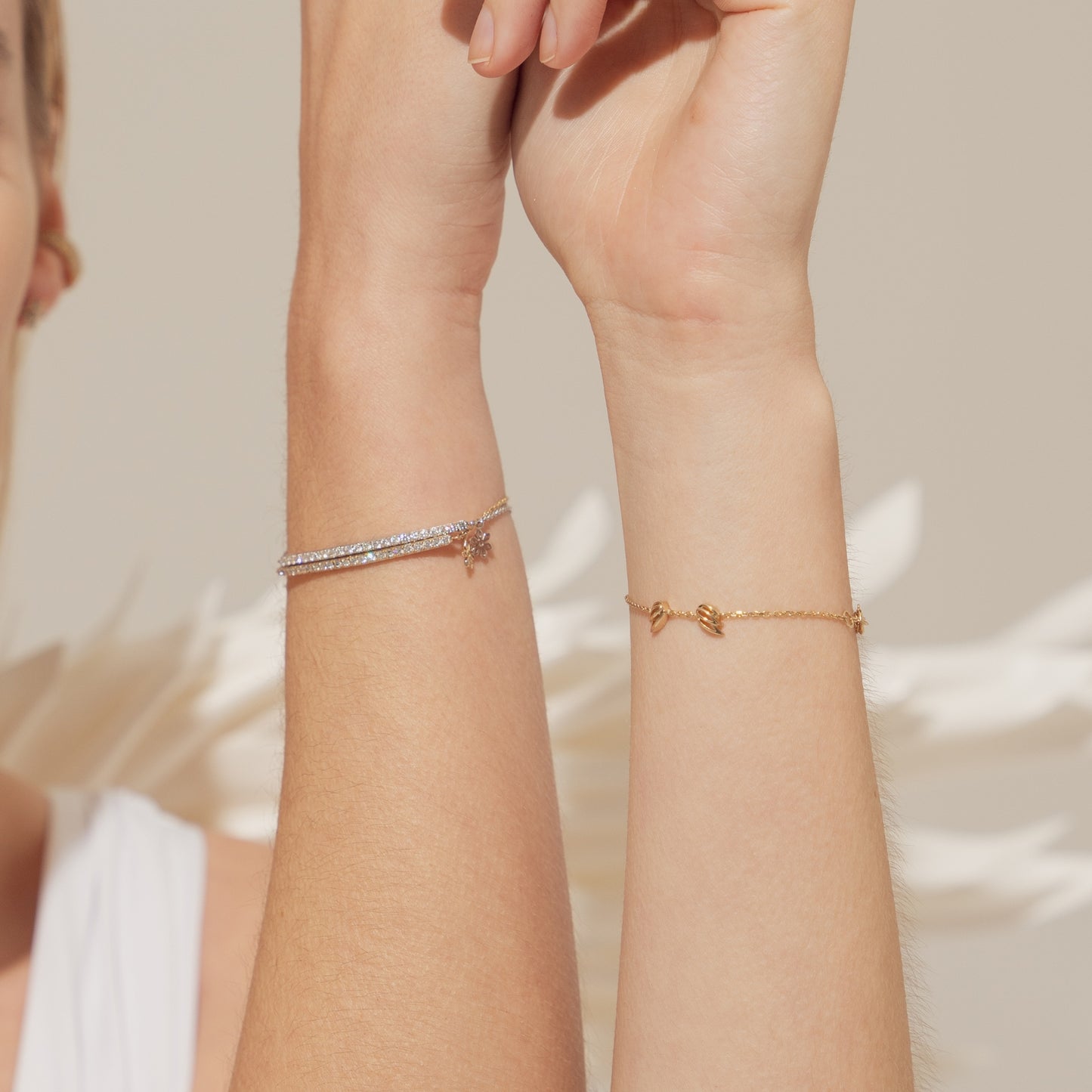 Two wrists wearing delicate bracelets on a neutral background. A detailed-macro-close-up of the-Illuminess-bar-bracelet, showcasing the-21-round-brilliant-lab-diamonds with VVS-clarity. The-image-highlights the-secure-setting and the-rich-blushing-hue of the-14K-solid-gold sourced-from-Swiss-refineries. This-view-emphasizes-extraordinary-craftsmanship and the-superior-light-refraction of the-premium-gemstones.