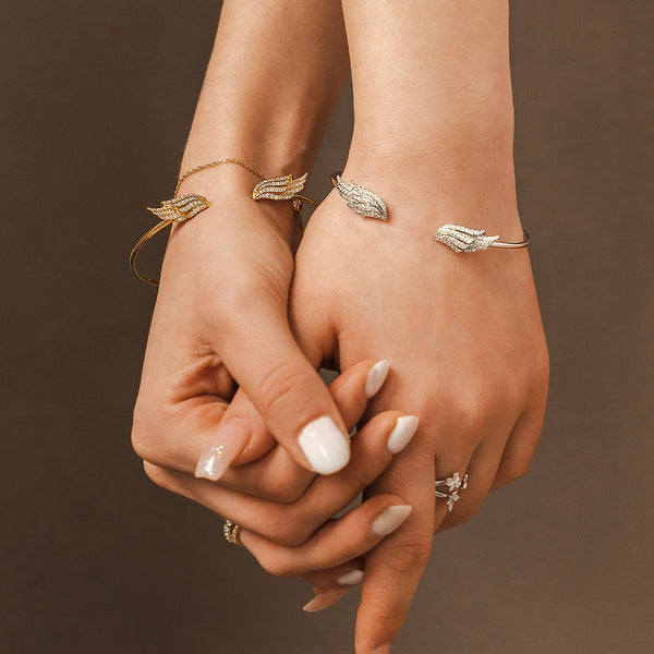 A lifestyle shot of two ladies modeling BLOOMTINE gold vermeil angel wing bracelets with lab-grown moissanites. This imagery highlights the tarnish-resistant gold luster and the spiritual talisman design, perfect for meaningful friendship or sisterhood jewelry gifts