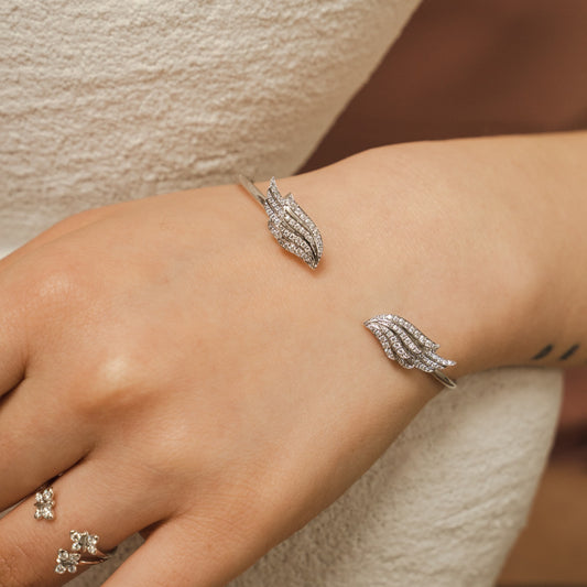 Angel Wing Sterling Silver Bangle image 1. A BLOOMTINE Angel Wing Bangle in premium White Rhodium-plated Sterling Silver. Featuring 98 hand-set lab moissanites across two sculptural wings, this flexible open-cuff design creates a 360-degree cosmic fire, serving as a symbolic talisman for protection and grace