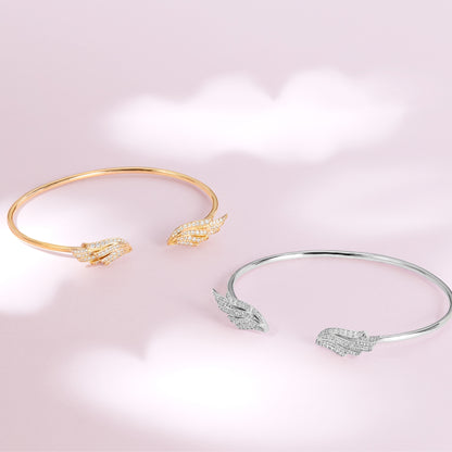 Two gold and silver bangles with feather designs on a pink background. Flexible open-wing sterling silver bangle by BLOOMTINE, set with 98 ethically sourced lab moissanites. This tarnish-resistant, hypoallergenic bracelet features a mirror-like rhodium finish and an innovative clasp-free fit, making it a premium milestone gift for 'Extraordinary Humans