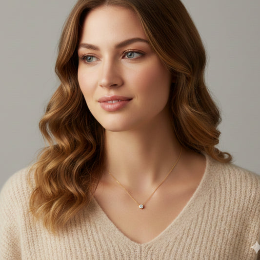 Close-up of a delicate BLOOMTINE gold pendant necklace on a model. This minimalist goddess-inspired accessory features a small, captivating charm on a fine gold-over-silver chain, demonstrating tarnish-resistant everyday luxury against a soft neutral backdrop