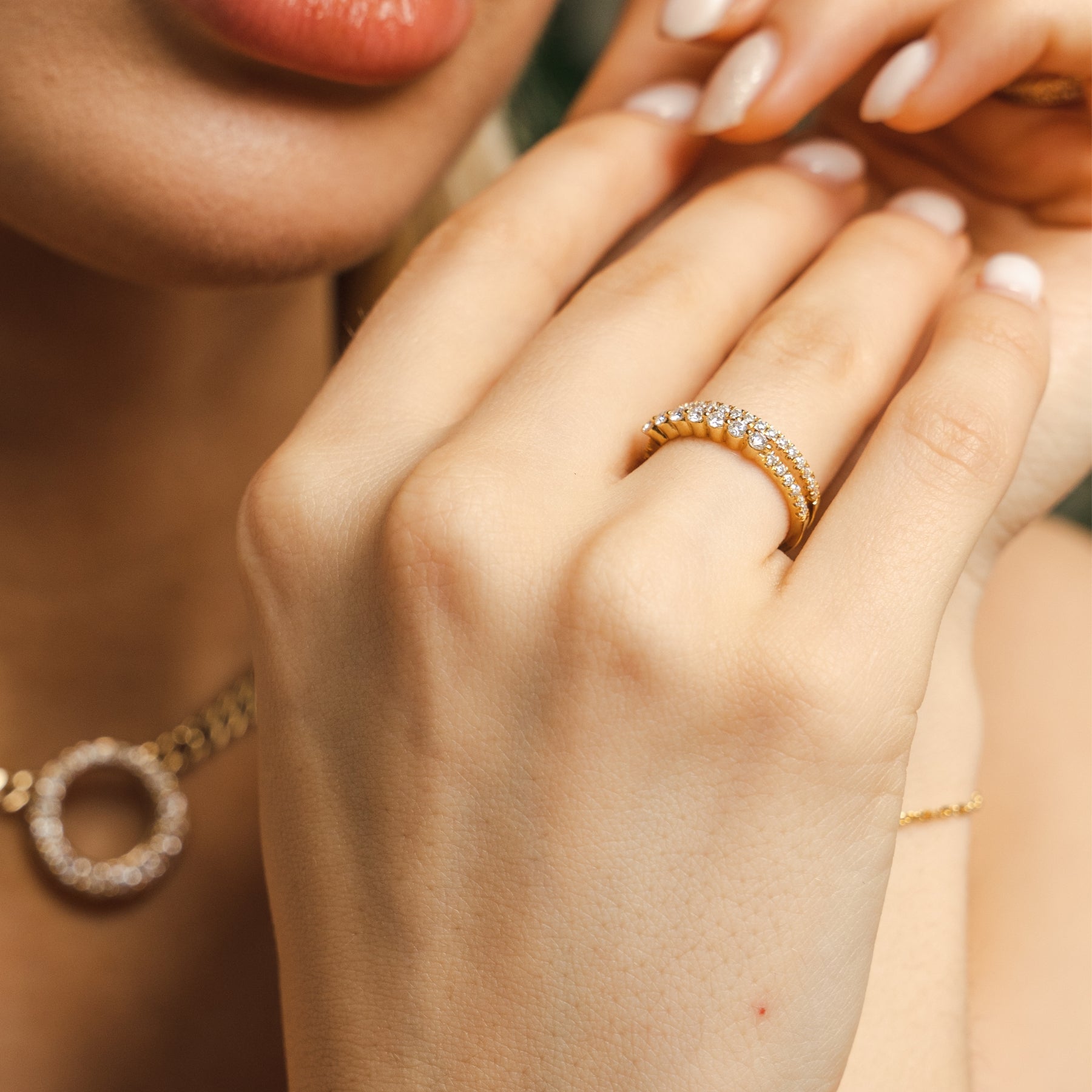 Close-up of a hand wearing a gold ring with a diamond band, with another hand touching the fingers. A signature BLOOMTINE 925 Sterling Silver Combi Ring featuring brilliant-cut lab-grown moissanites. This innovative dual-band design provides the look of a curated ring stack, handcrafted for durability and cosmic sparkle, exclusively available at BLOOMTINE, Wolf & Badger, and House of Fraser